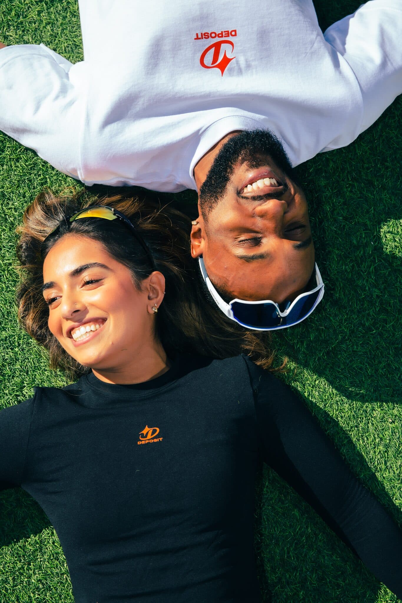 Two people lying on turf, heads together.