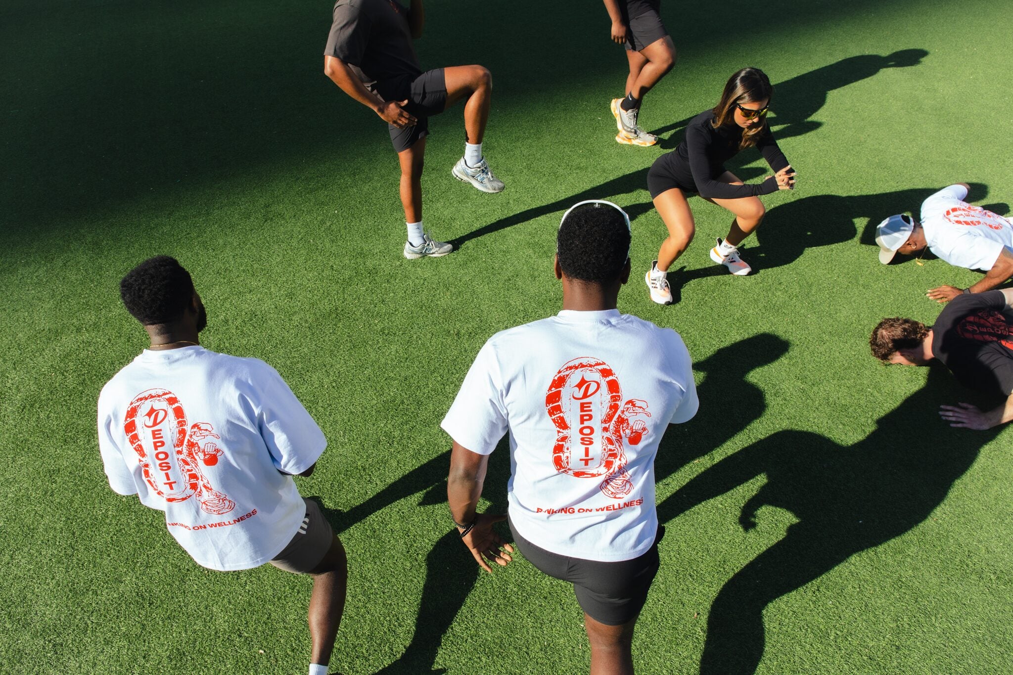 Overhead view of a group stretching on turf in Banking on Wellness tees.